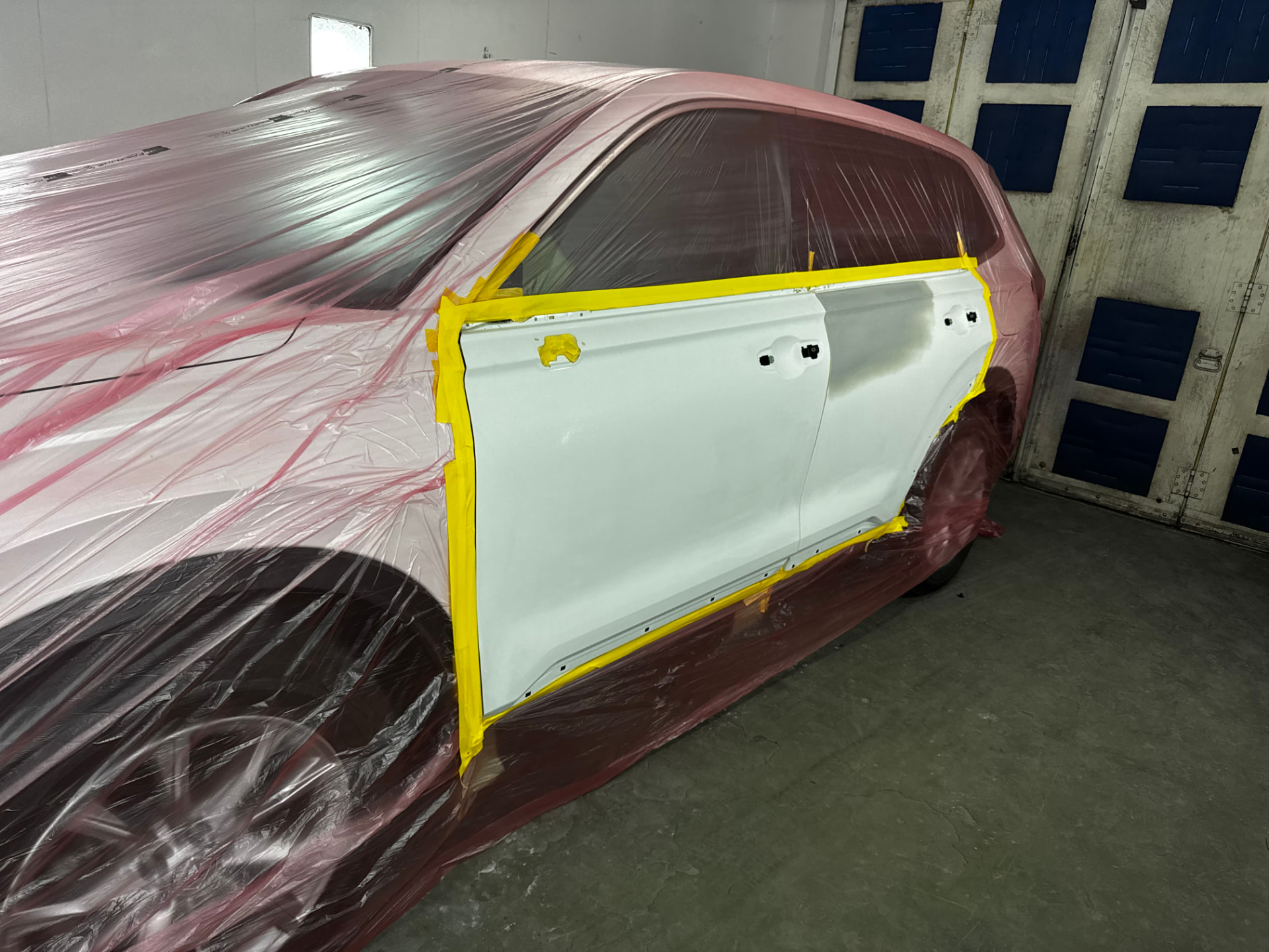 Replacement door panel masked for paint on a red SUV in the booth