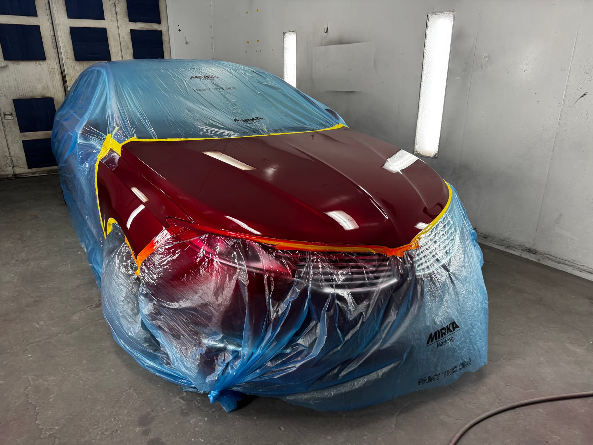 Freshly painted deep red hood on a sedan being refinished in the paint booth